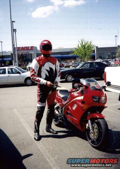Red motorcycle with a rider in matching leathers, parked in a lot