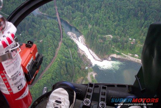 Helicopter interior with red fire extinguisher, view of waterfall, river, bridge, and forest