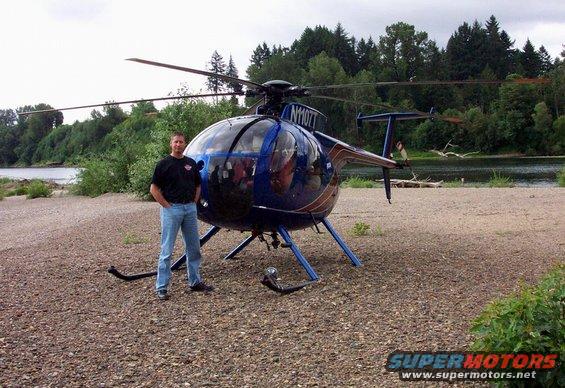 Man standing next to a blue helicopter on a gravelly shore