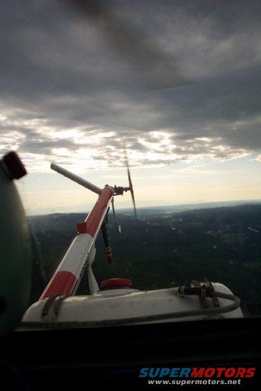 View from inside a helicopter looking out at the rotor and landscape below