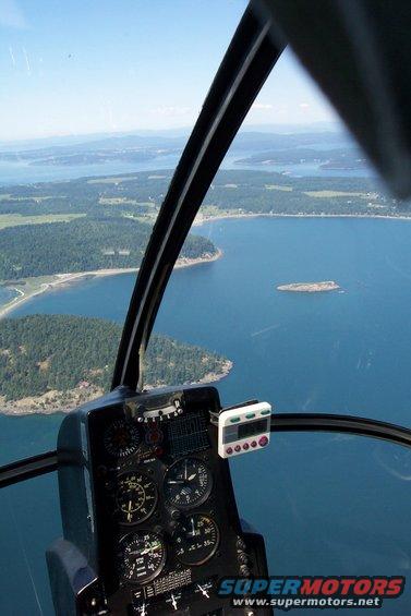 Helicopter cockpit interior with gauges and a view of a coastline and islands