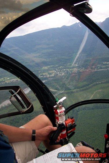 Helicopter interior view of mountains and town below, with controls and fire extinguisher visible