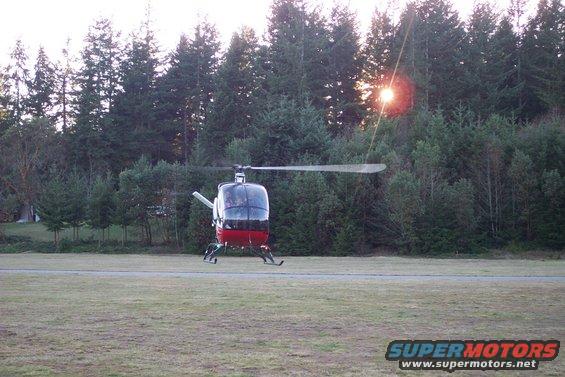 Red and black helicopter on a grassy field with trees in the background