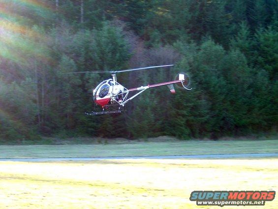 helicopter flying over grassy field with trees in background
