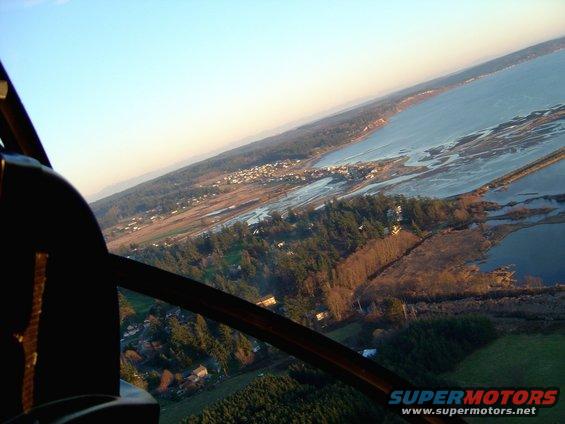 Helicopter cockpit view over a coastal town and bay at sunset