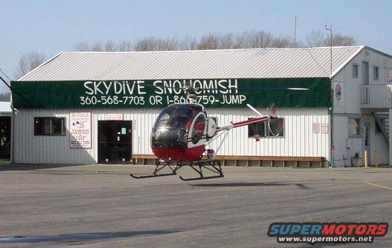 Red and black helicopter on tarmac in front of Skydive Snohomish building