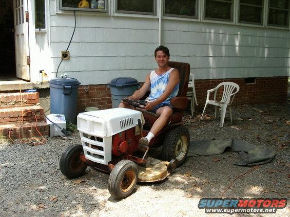 Guy sitting on a red and white riding lawn mower in a yard