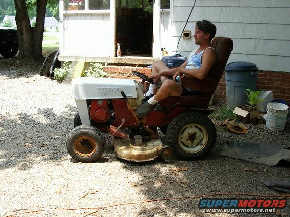 Man on red and white riding lawn mower, side view
