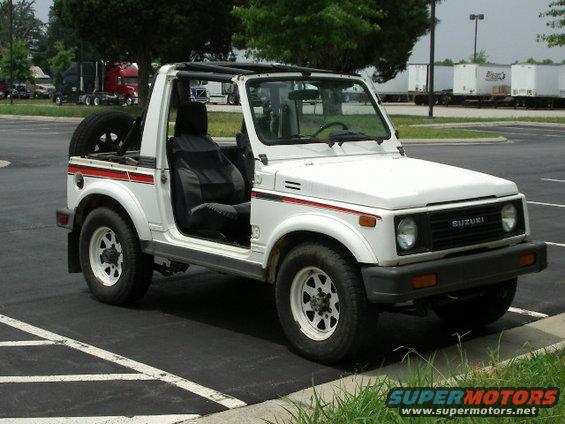 White Suzuki Samurai convertible with black interior and spare tire on back, parked on asphalt