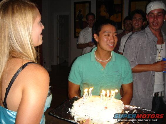 People gathered around a cake with lit candles, indoors