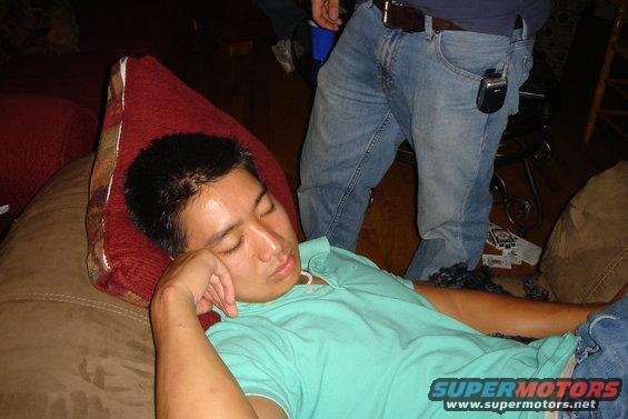 Man sleeping on a brown couch, wearing a teal polo shirt and blue jeans