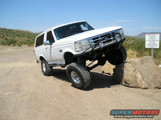White Ford Bronco with lifted suspension and off-road tires climbing a rock