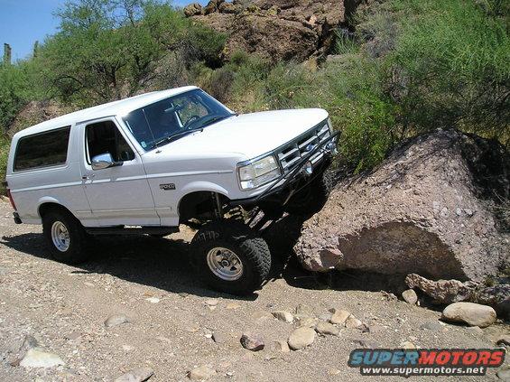 White Ford Bronco with lifted suspension navigating a large rock on a dirt trail