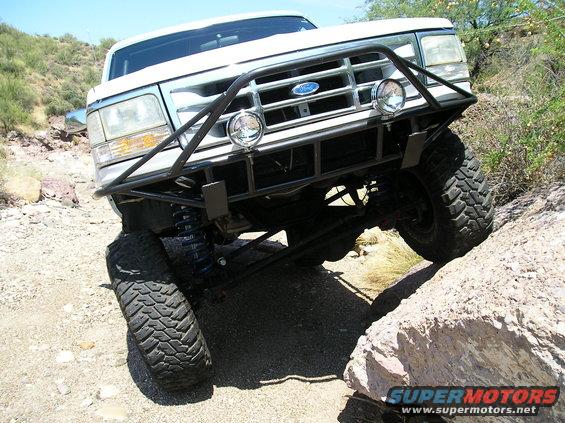 Ford truck with aftermarket bumper and lights climbing over rocks