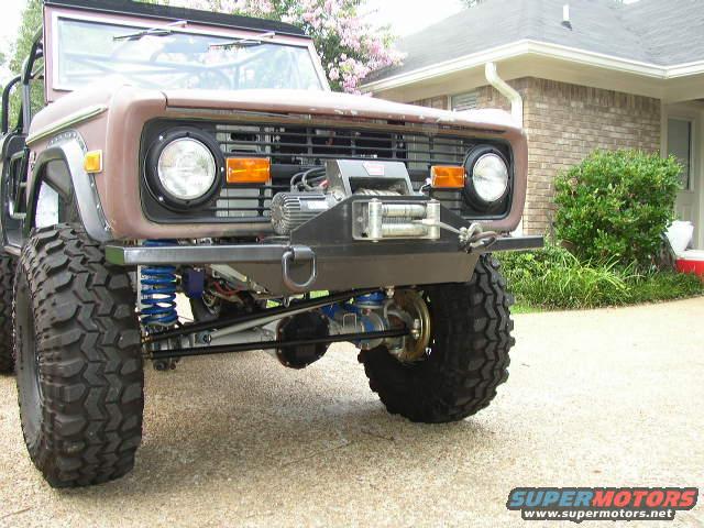 1978 Ford Bronco front end with custom bumper and winch. Large off-road tires and blue suspension components are visible