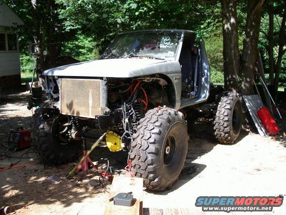 Off-road truck with large tires, missing front clip and engine exposed, on jacks