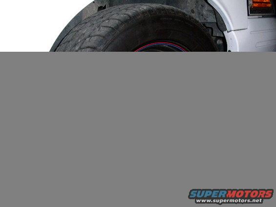 Wheel well and tire of a white vehicle, showing wear on the tire tread and a red and blue stripe on the wheel rim