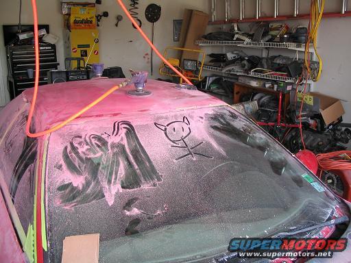 Red car body covered in pink dust, with a drawing of a devil on the windshield