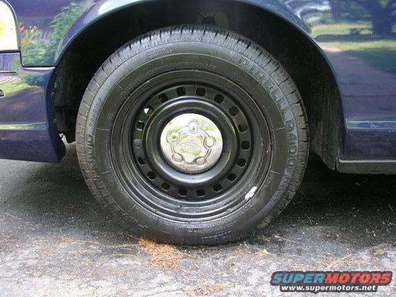 Close-up of a dark blue car's steel wheel with a chrome hubcap and Pirelli tire. The fender is visible above the wheel