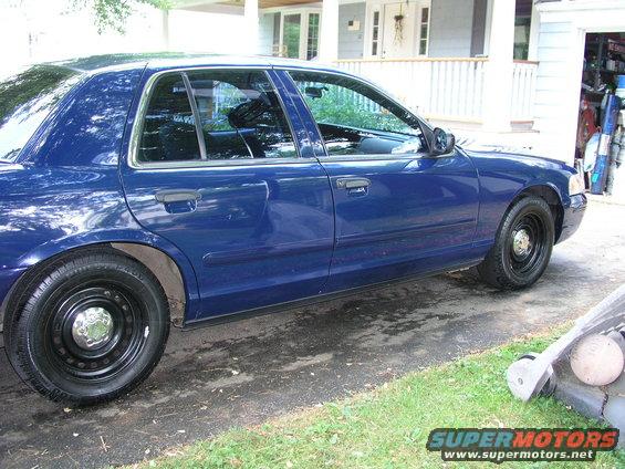 Blue sedan with black steel wheels, chrome hubcaps, and black trim. Visible damage on the rear passenger door