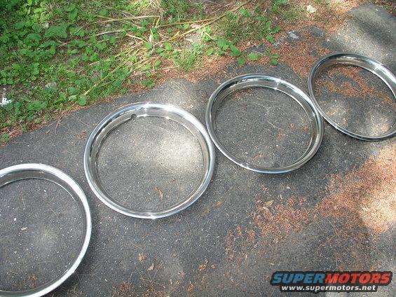 Four chrome trim rings on asphalt with grass in background