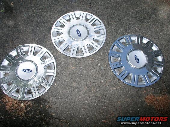 Three Ford wheel covers on a dark, textured surface. Two are identical, one is slightly different