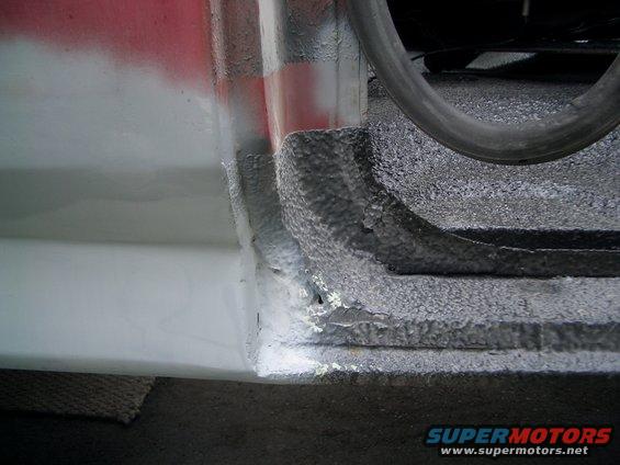 close-up of vehicle door sill showing undercoating and some red paint overspray