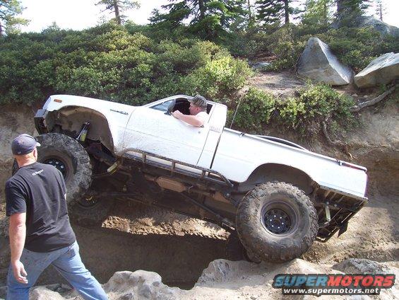 White pickup truck with large tires navigating a steep dirt incline, driver visible