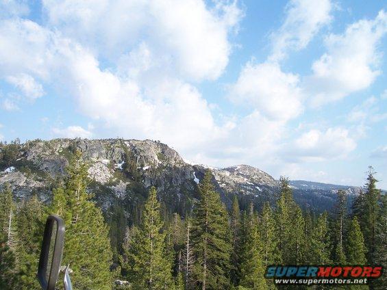 View from a vehicle looking out at a mountain range covered in trees and some snow