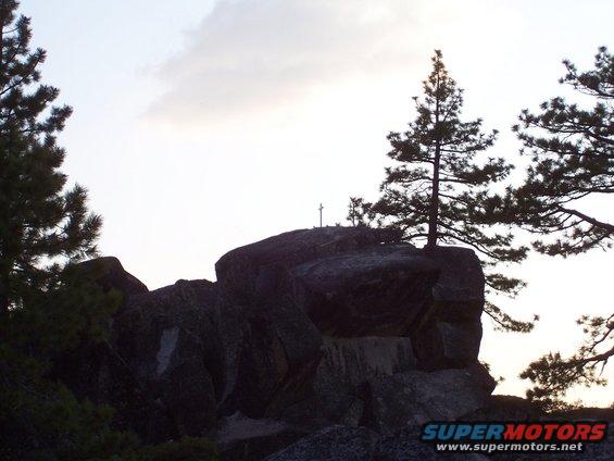 Rocky outcrop with trees and a cross against a cloudy sky