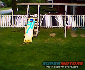 Drawing of a blue stick figure with red eyes on a yellow slide in a backyard with a white picket fence and swing set