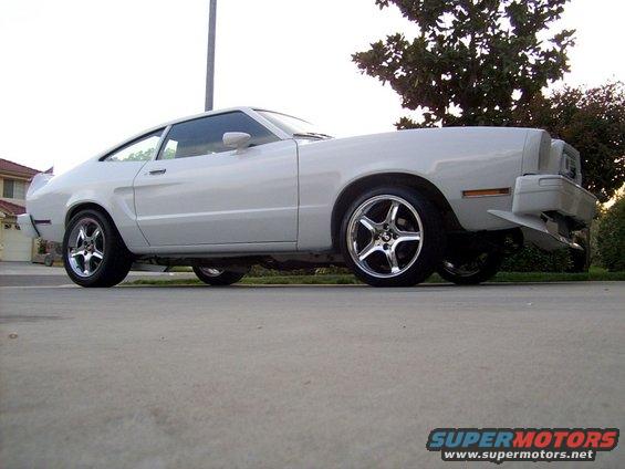White coupe car with aftermarket wheels, seen from the side at a low angle