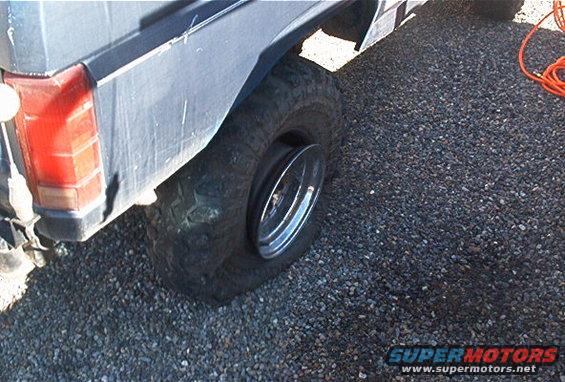Flat tire on a vehicle, showing the rear taillight and wheel well