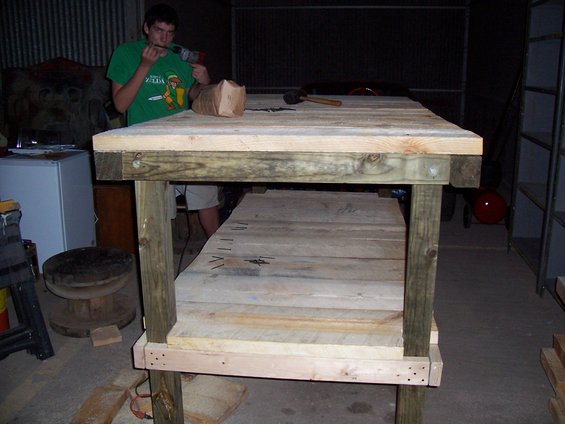 Person using a drill on a wooden workbench, with lumber and tools visible
