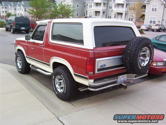 Red and white 1986 Ford Bronco rear quarter view with spare tire