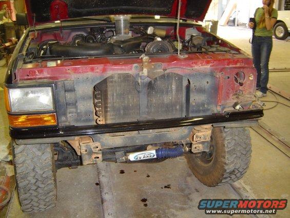 Front of red pickup with hood open, showing engine and radiator. Aftermarket shocks visible