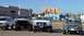 1995 Ford Bronco - A lineup of four lifted trucks, including a white Ford F-Series, are parked outdoors under a clear blue sky.