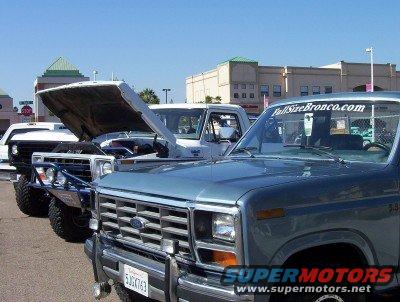 Blue 1980s Ford Bronco front end with chrome grille, bumper, and license plate. Other trucks are behind it