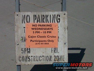 Wooden sign with 'NO PARKING' and an orange insert detailing 'NO PARKING WEDNESDAYS 5 PM - 10 PM Cajon Classic Cruise Participants Only (619) 401-8858'