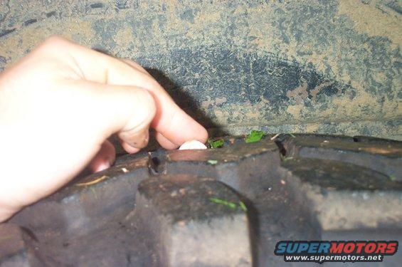 Hand pressing on a piece of debris stuck in tire tread