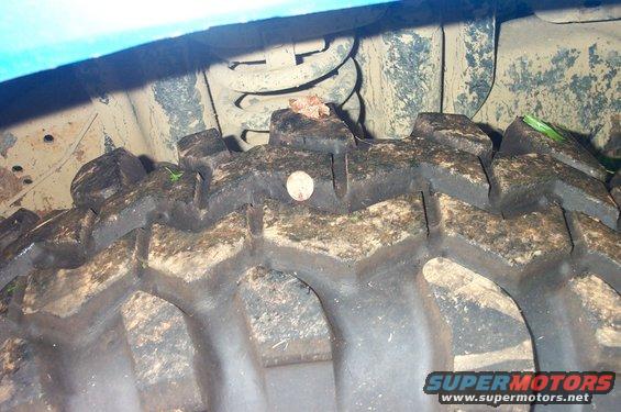 Close-up of a muddy off-road tire with a nail in it. Suspension parts are visible above