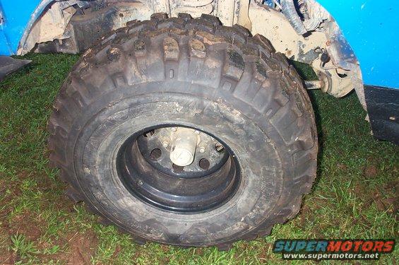 Close-up of a large, knobby off-road tire on a black rim, with part of a blue vehicle body visible