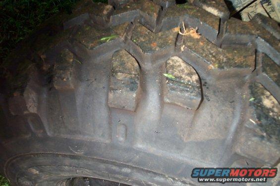 Close-up of a muddy tire tread with visible SuperMotors logo