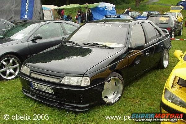Black sedan with custom wheels parked on grass next to a dark gray car and a yellow car