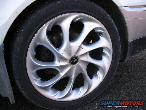 Close-up of a silver alloy wheel with a black tire and a circular logo in the center