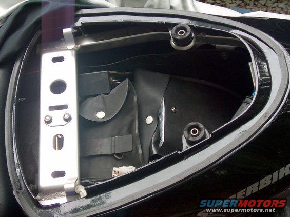Motorcycle tail section open, showing black storage compartment with a metal bracket and a folded black pouch inside