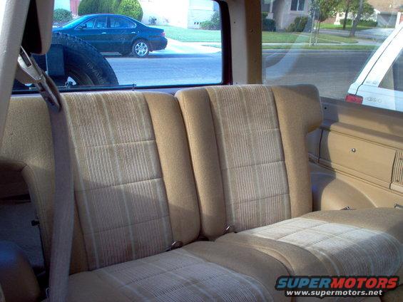 1985 Ford Bronco II interior showing rear seats and spare tire mounted behind driver's seat. Another vehicle is visible through the rear window