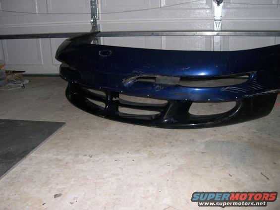 Blue car bumper with black lower grille, sitting on a concrete floor in a garage