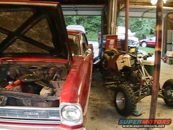 Red 1966 Chevrolet Nova with hood open, showing engine bay, parked next to an ATV in a garage