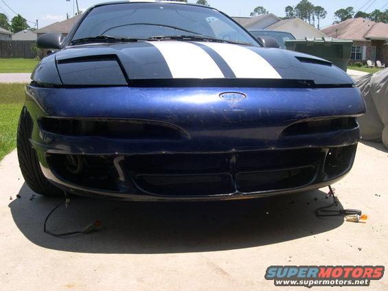 Front view of a blue car with white racing stripes on the hood. The bumper is partially removed